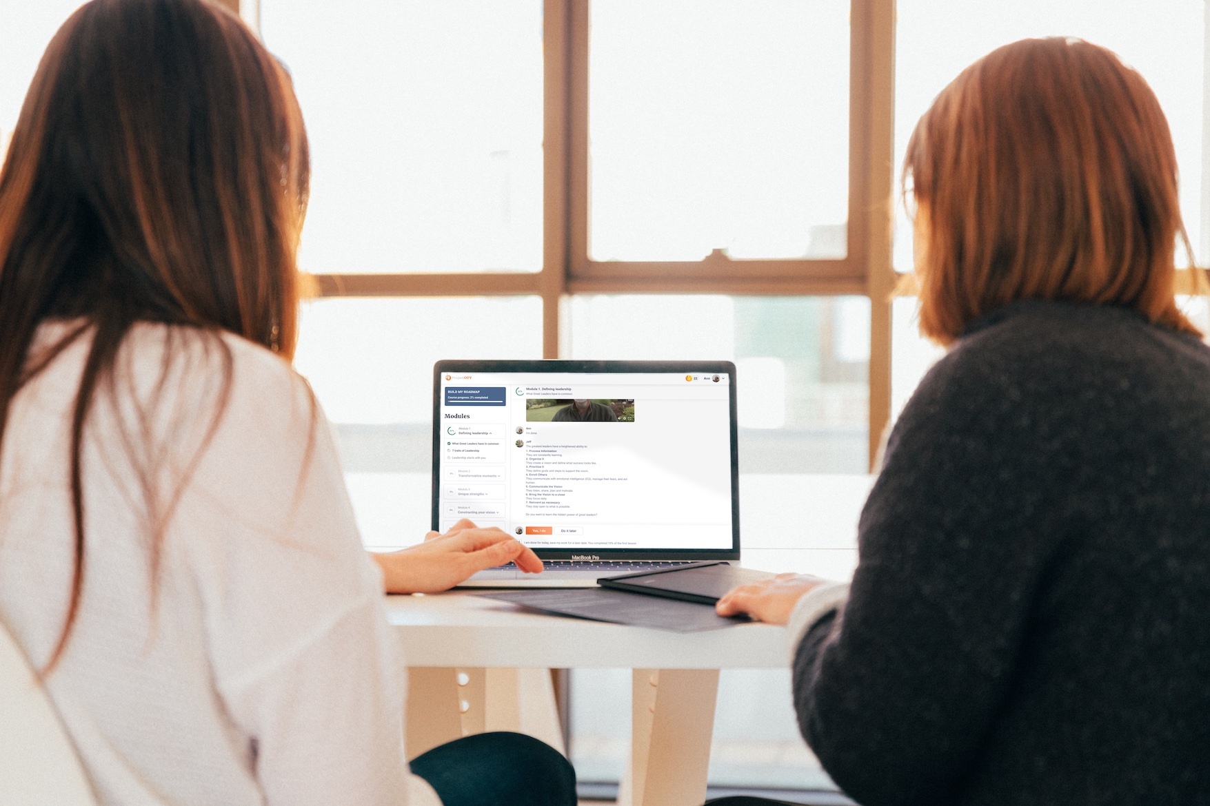 two women sitting by a window and looking at a laptop