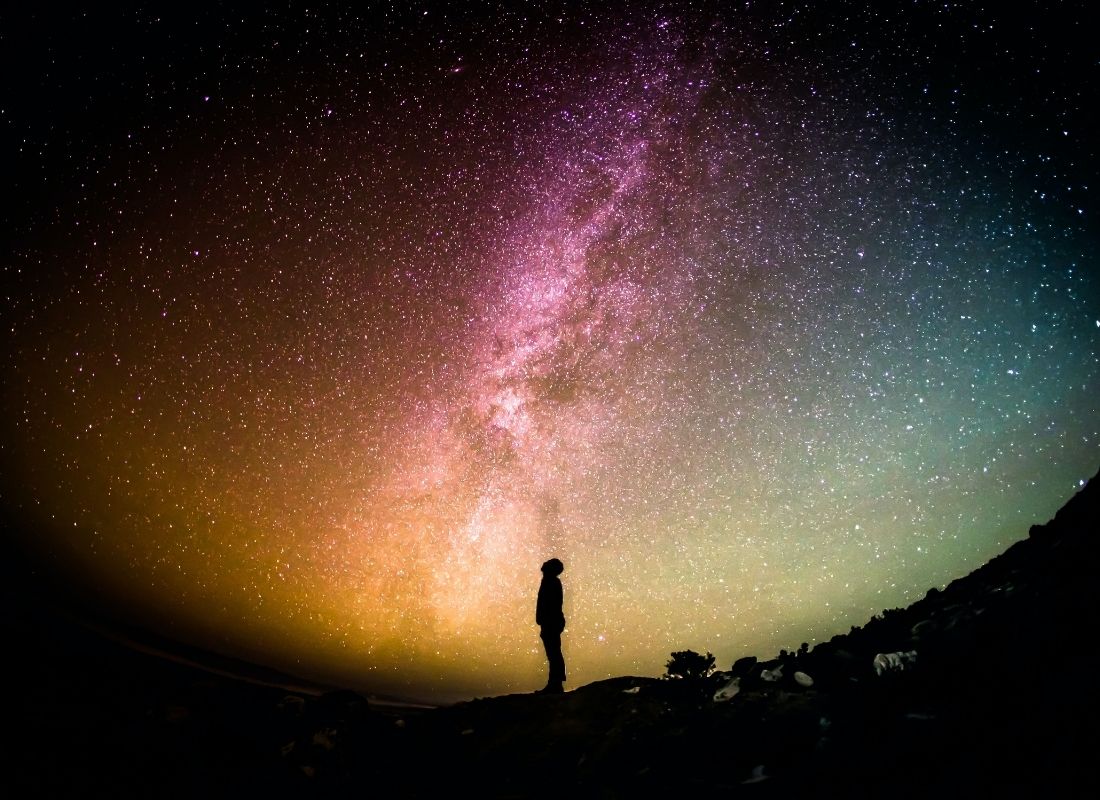 Person staring up at starry and colorful night sky