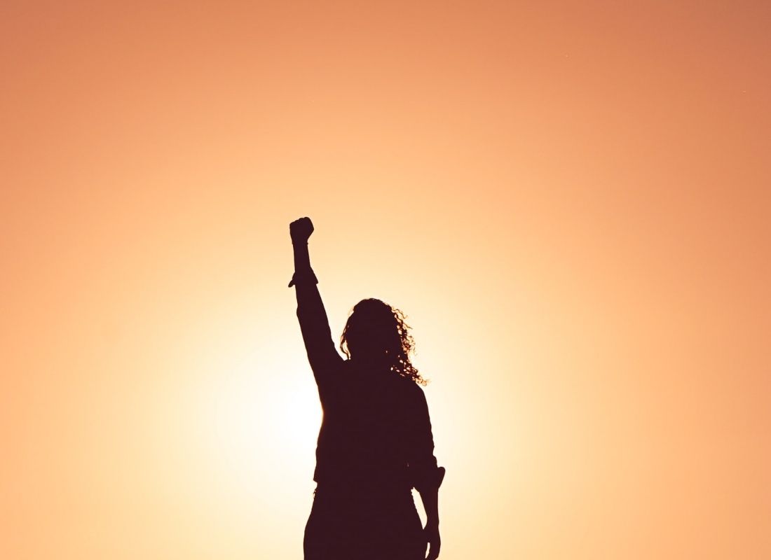 woman pumping fist in the air silhouette at sunset