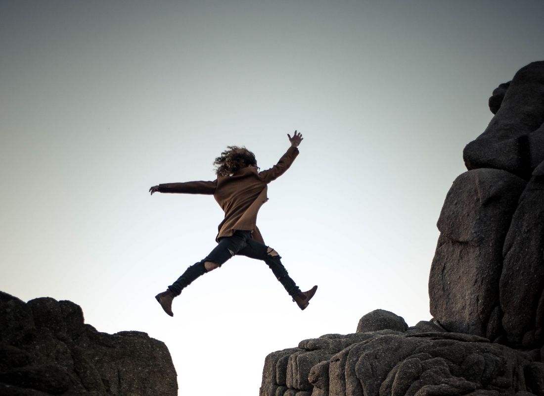 Woman conquering fear and jumping across rock cliffs