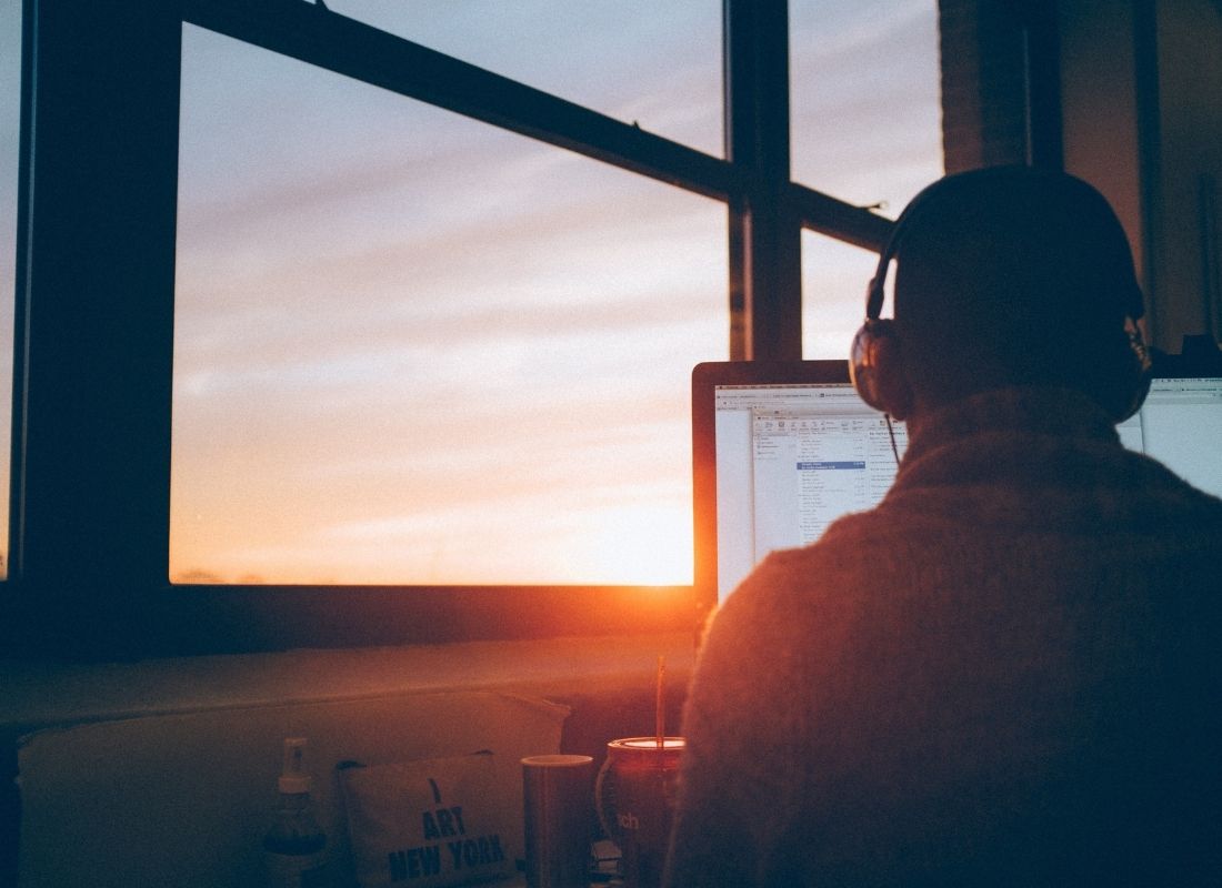 Man with headphones looking at computer at sunrise in deep consistent work