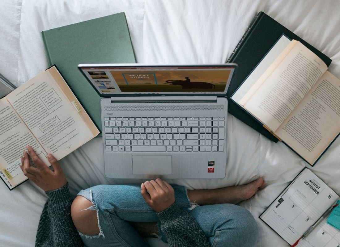 Person learning on a laptop with books around it on a bed