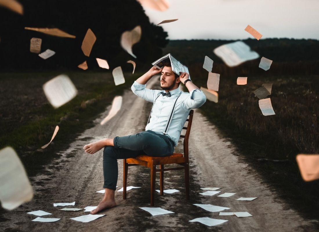 Man on chair on a road with papers falling around him