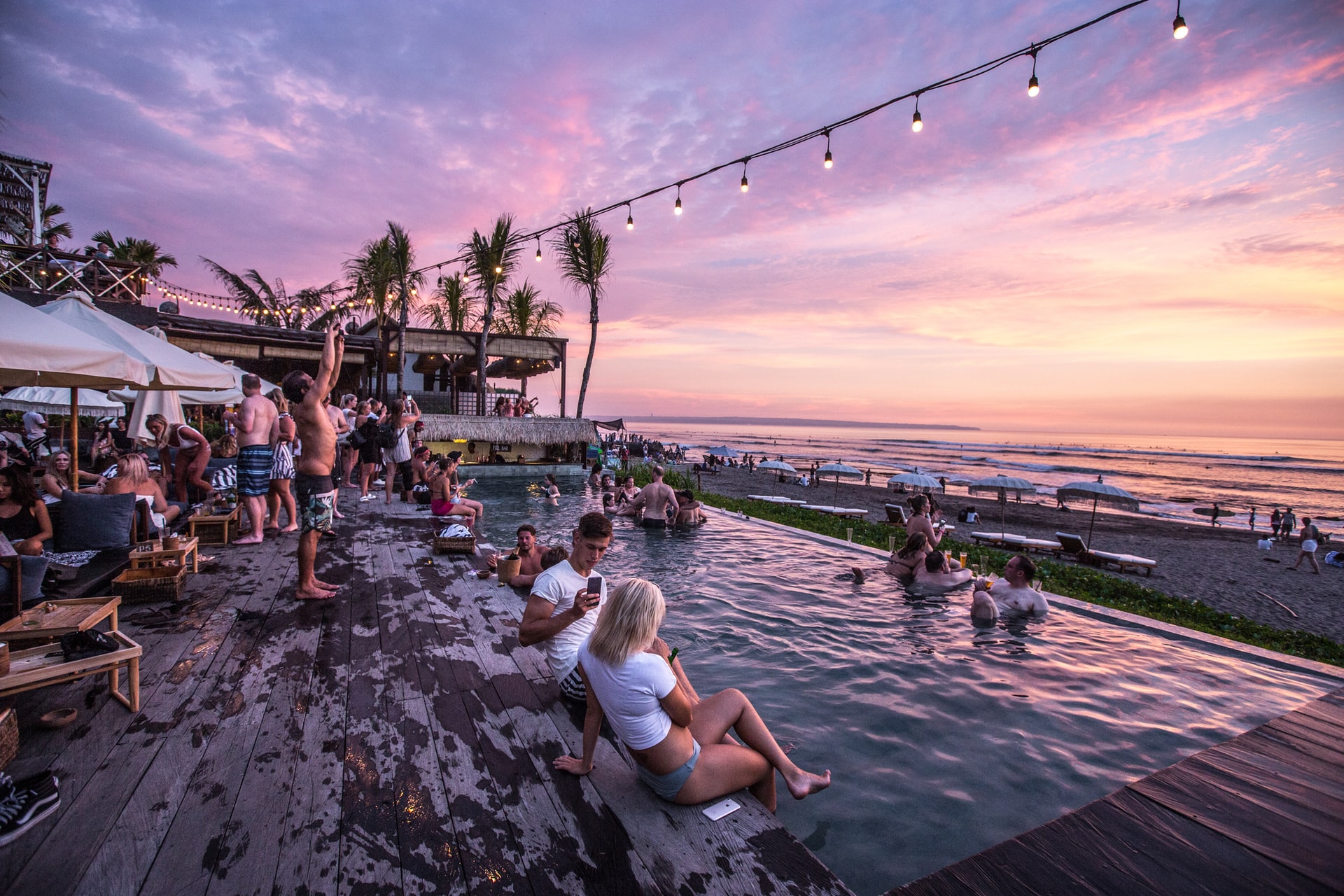 Image of adults in a swimming pool overlooking a beach at sunset