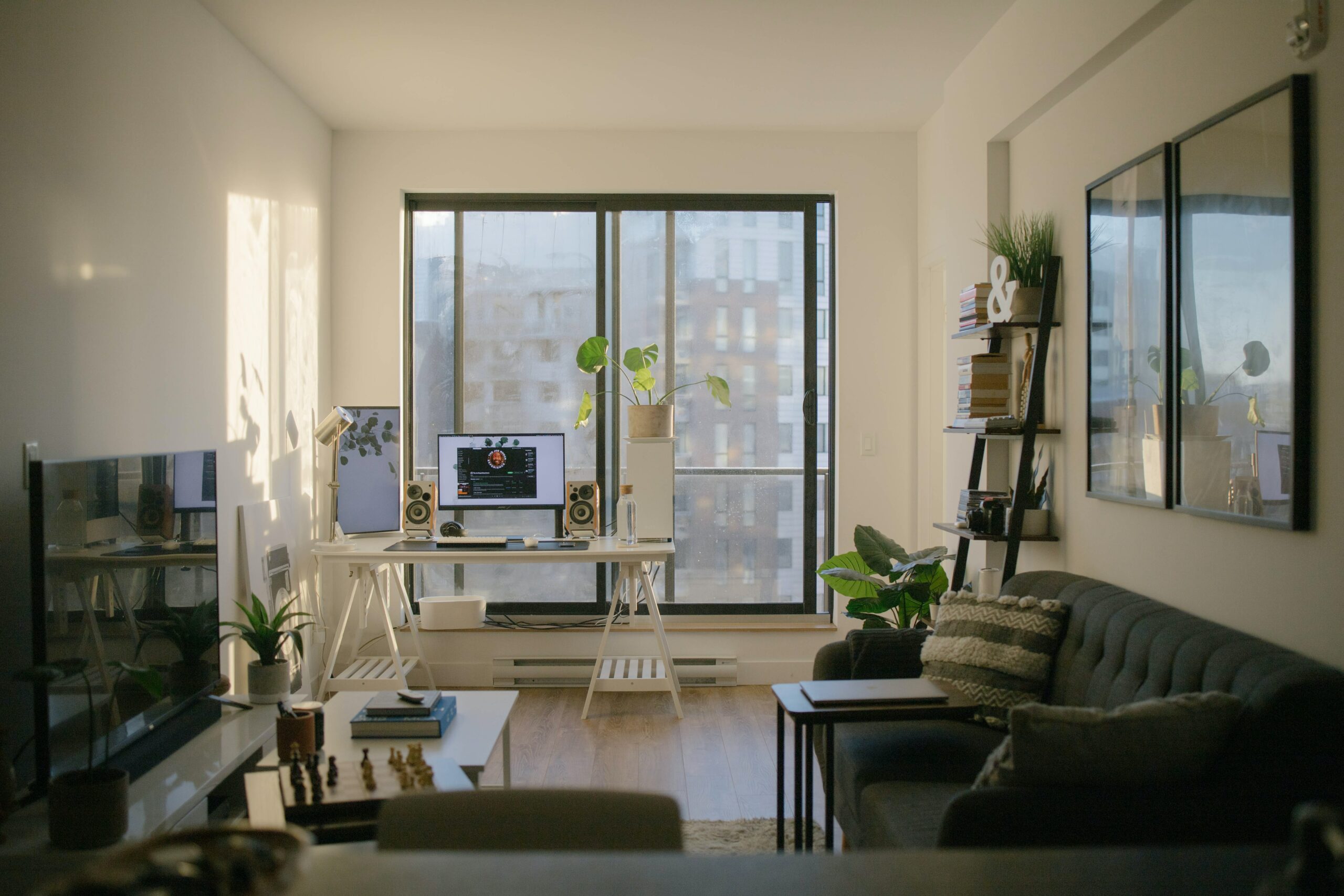 Image of a decorated apartment living room with a couch, television, desk setup and artwork overlooking a window with a city building view