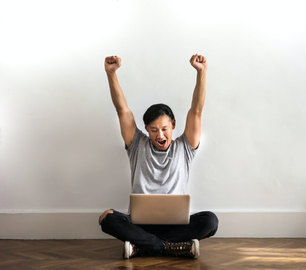 man sitting on the floor against a white wall with a laptop on his lap