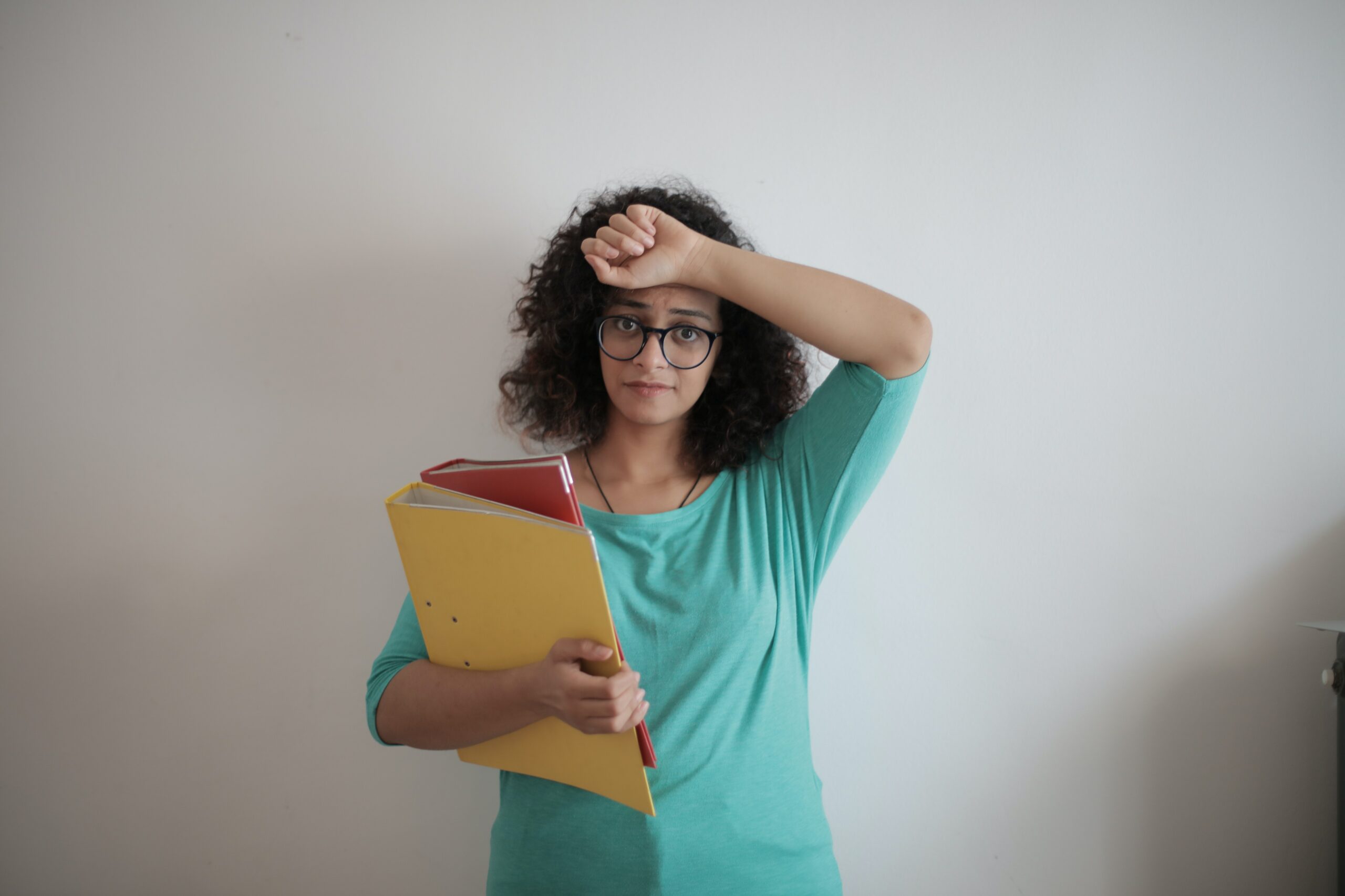 Image of a curly haired woman in a mint green shirt hold multi-colored binders