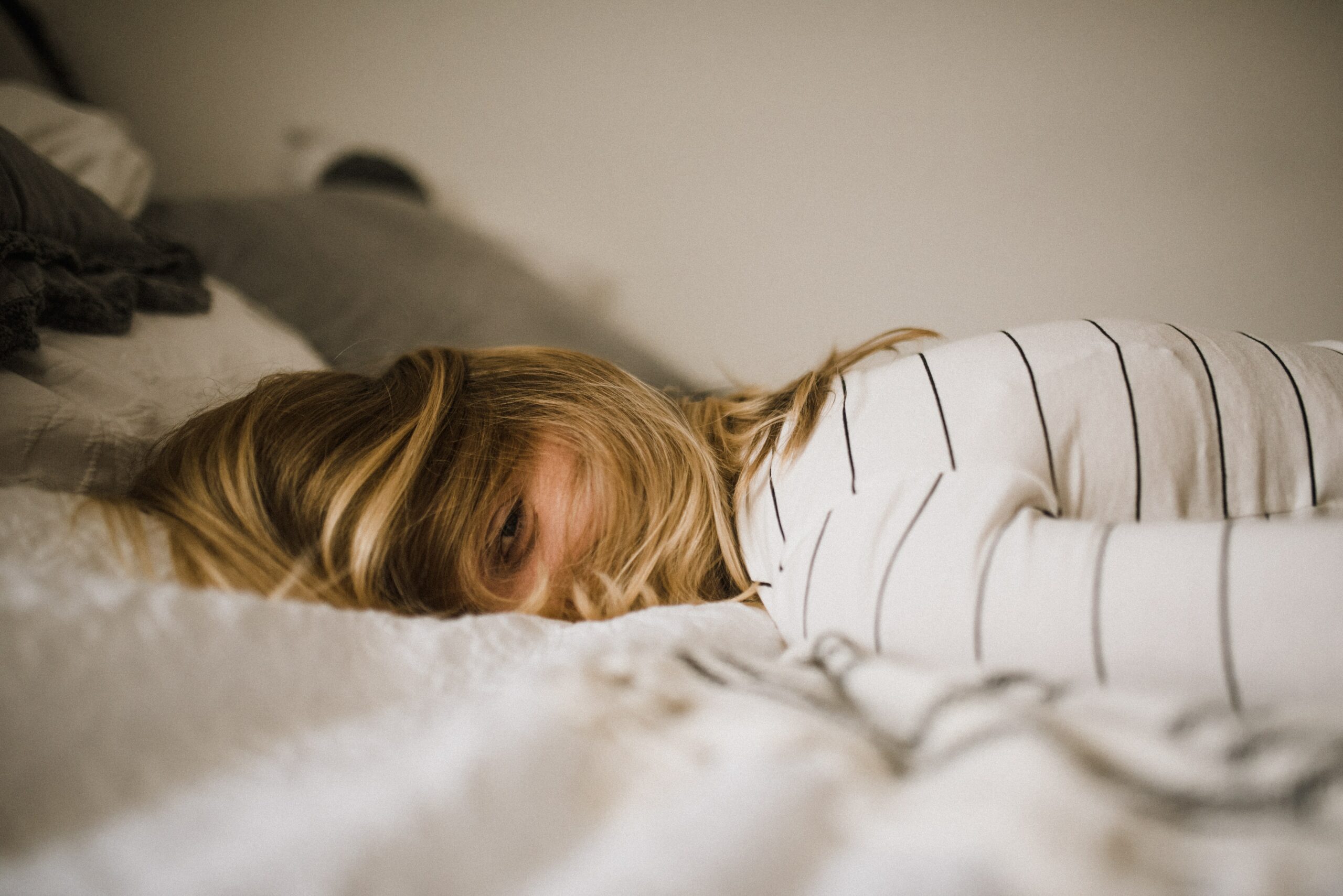 tired blonde woman lying on a white bed with a cover