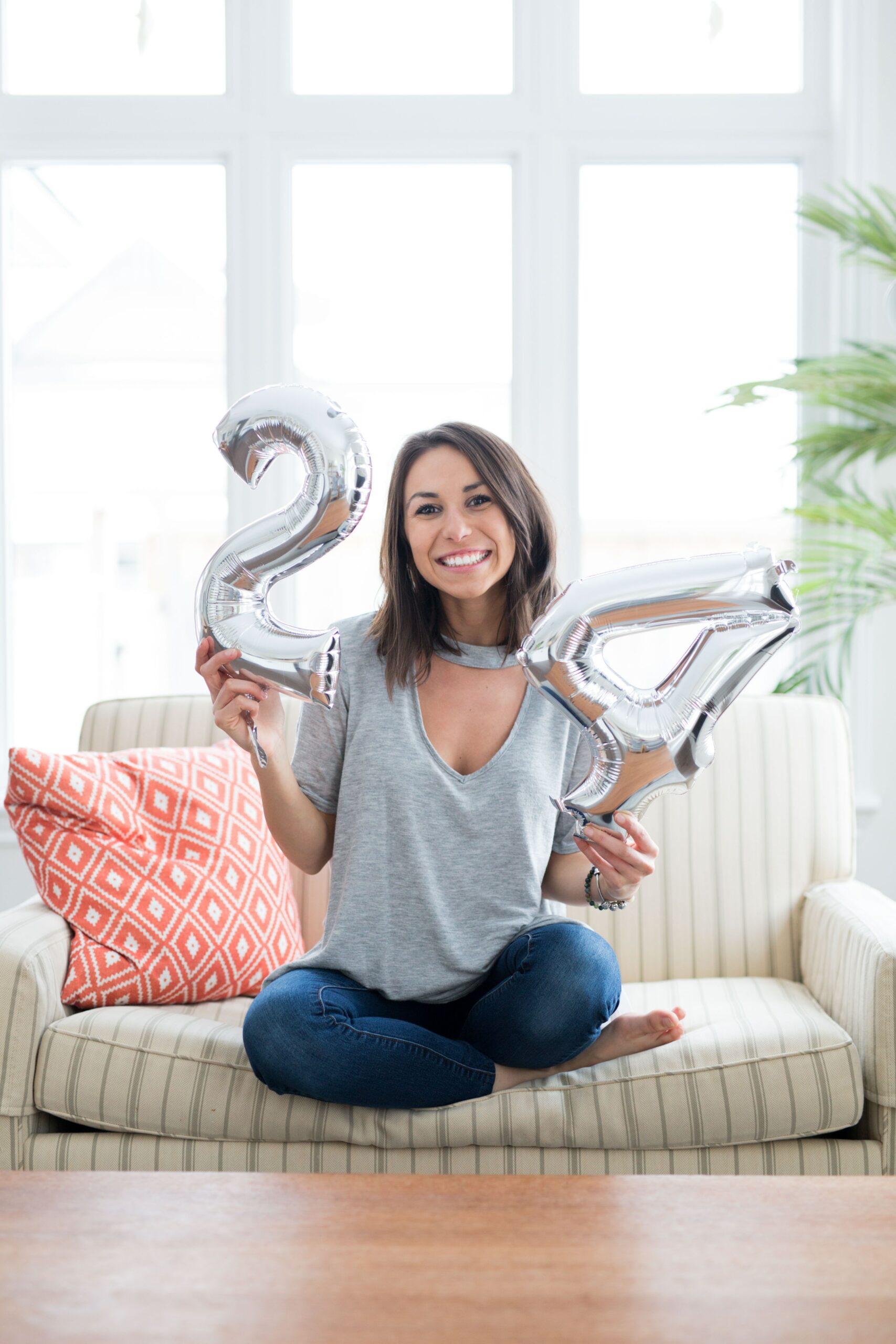 Brunette woman holding silver numbered balloons for her 24th birthday
