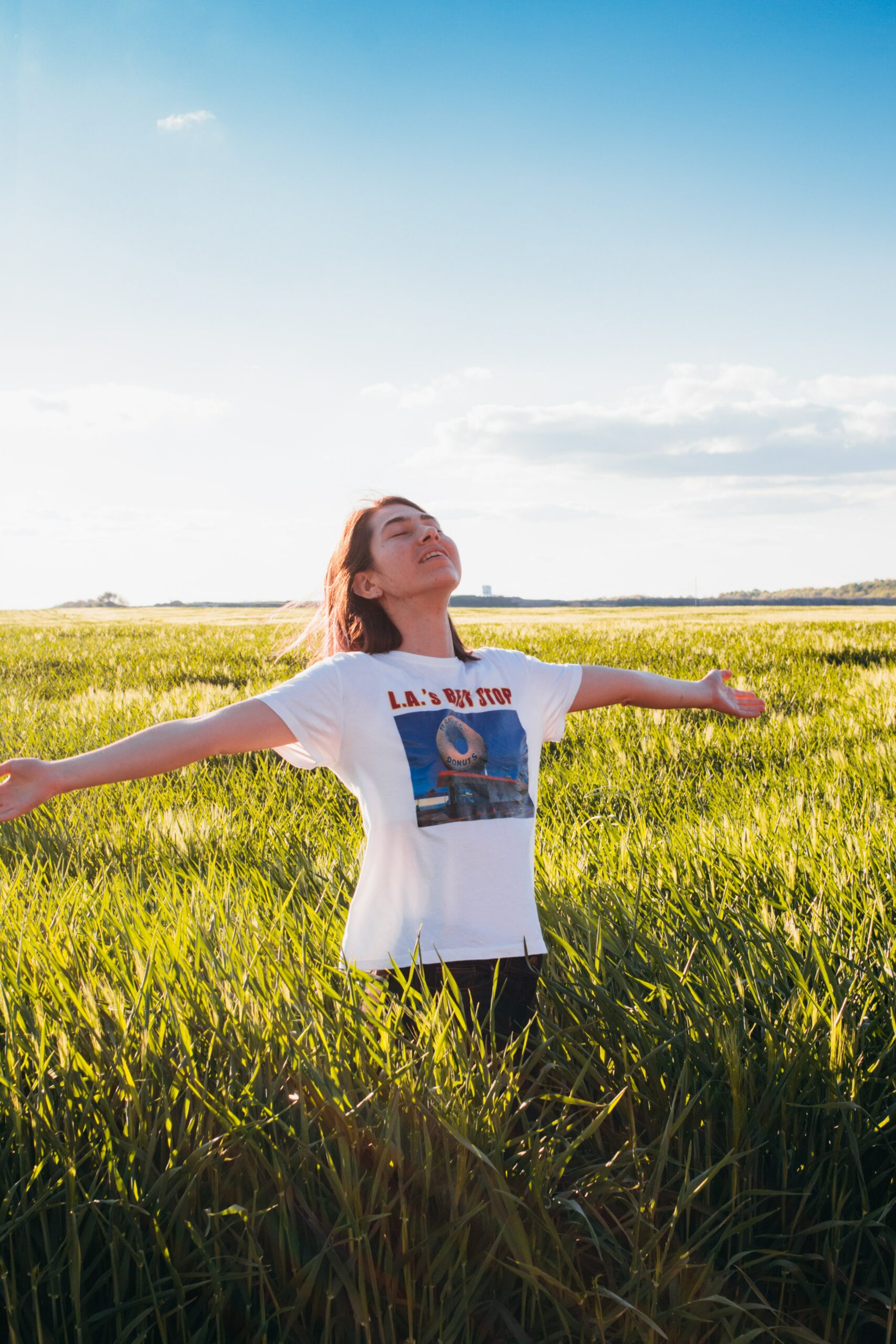 Smiling brunette in a white shirt standing in a grassy field with arms outstretched
