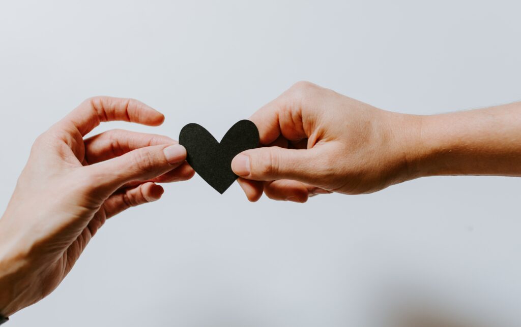 two hands holding a black paper cutout of a heart