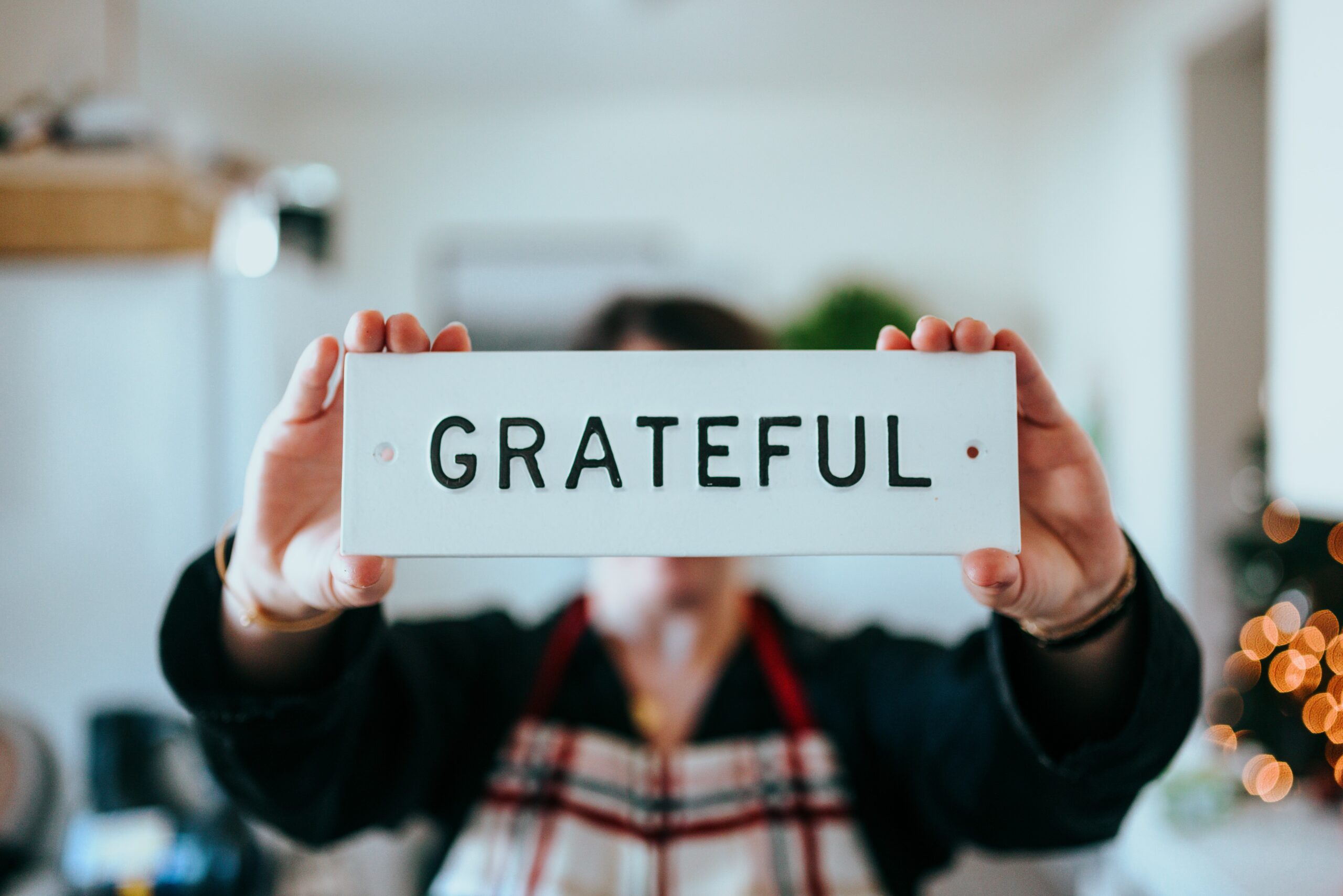 woman in an apron holding up a sign that says "grateful" in black text