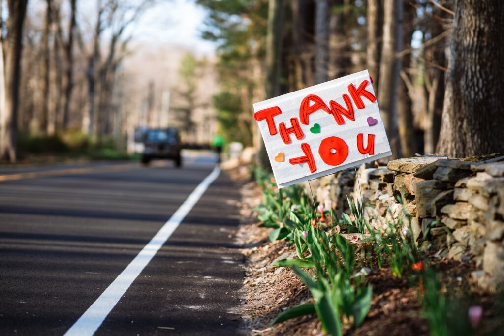 Sign with "thank you" in red text on the side of the road